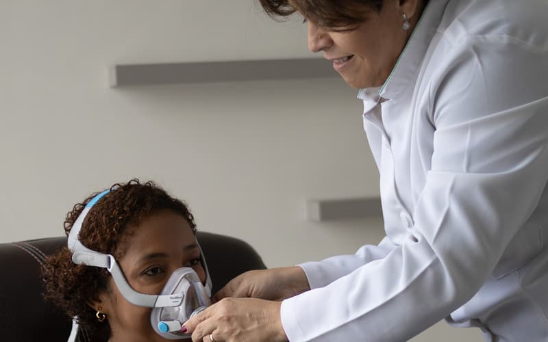 Fisioterapeuta da Sonofisio ajustando a máscara de CPAP no rosto de uma paciente