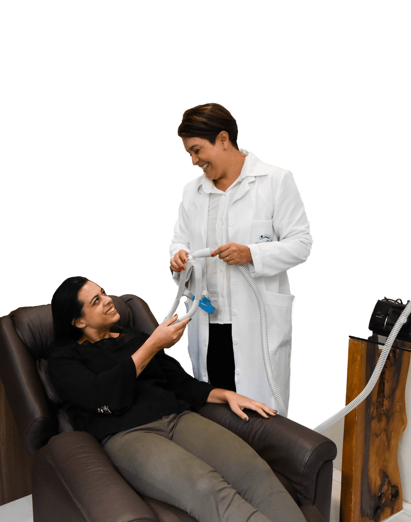 Fisioterapeuta da Sonofisio mostrando a máscara de CPAP a uma paciente sentada na poltrona